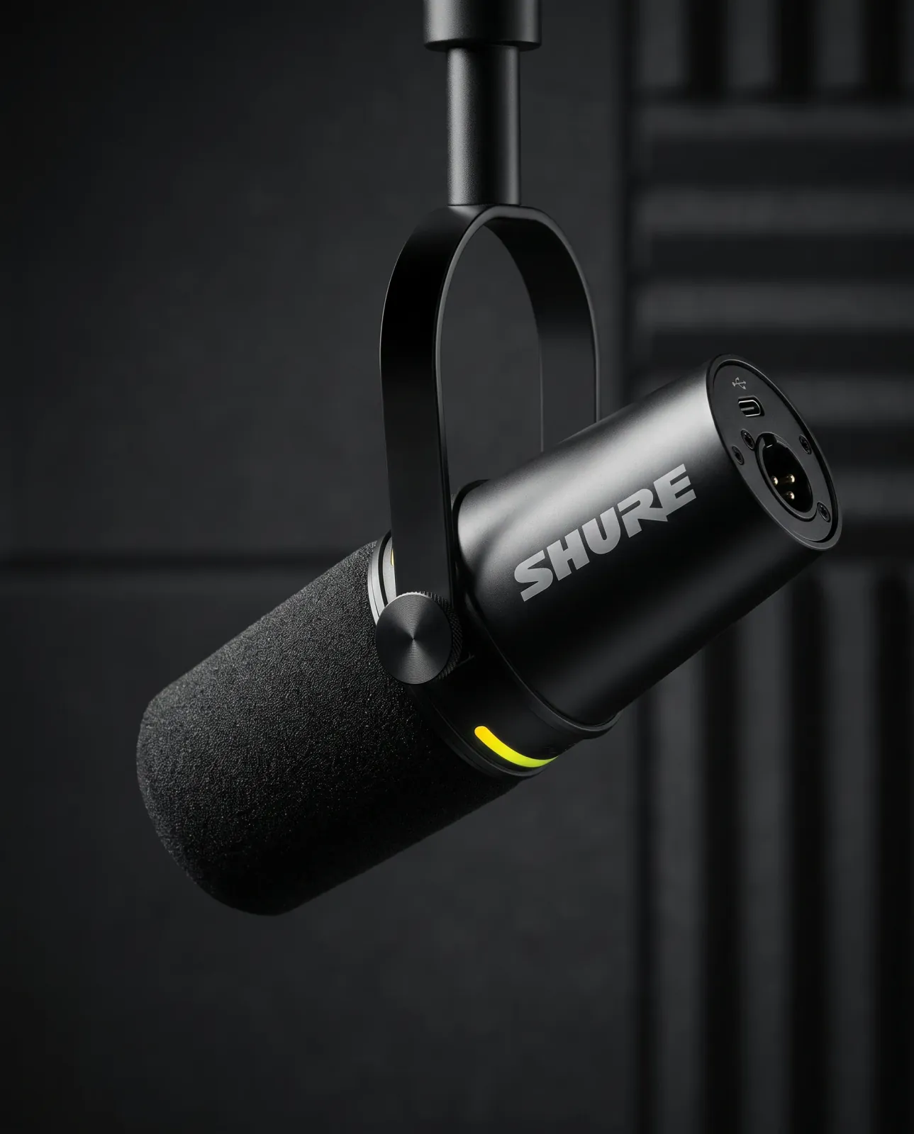 A close-up of the same black Shure MV7+ microphone in a dark premium editorial studio, with its rear connections visible.