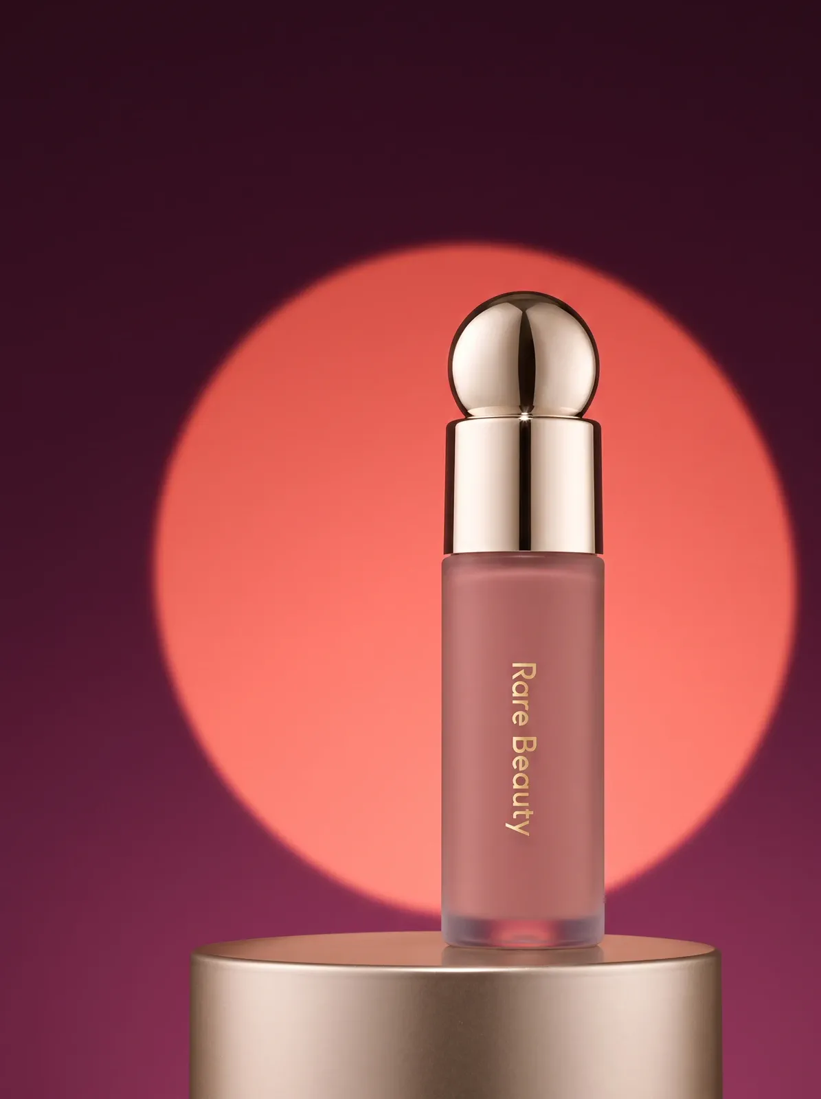 The same liquid blush bottle in a deep plum campaign scene with a coral spotlight.