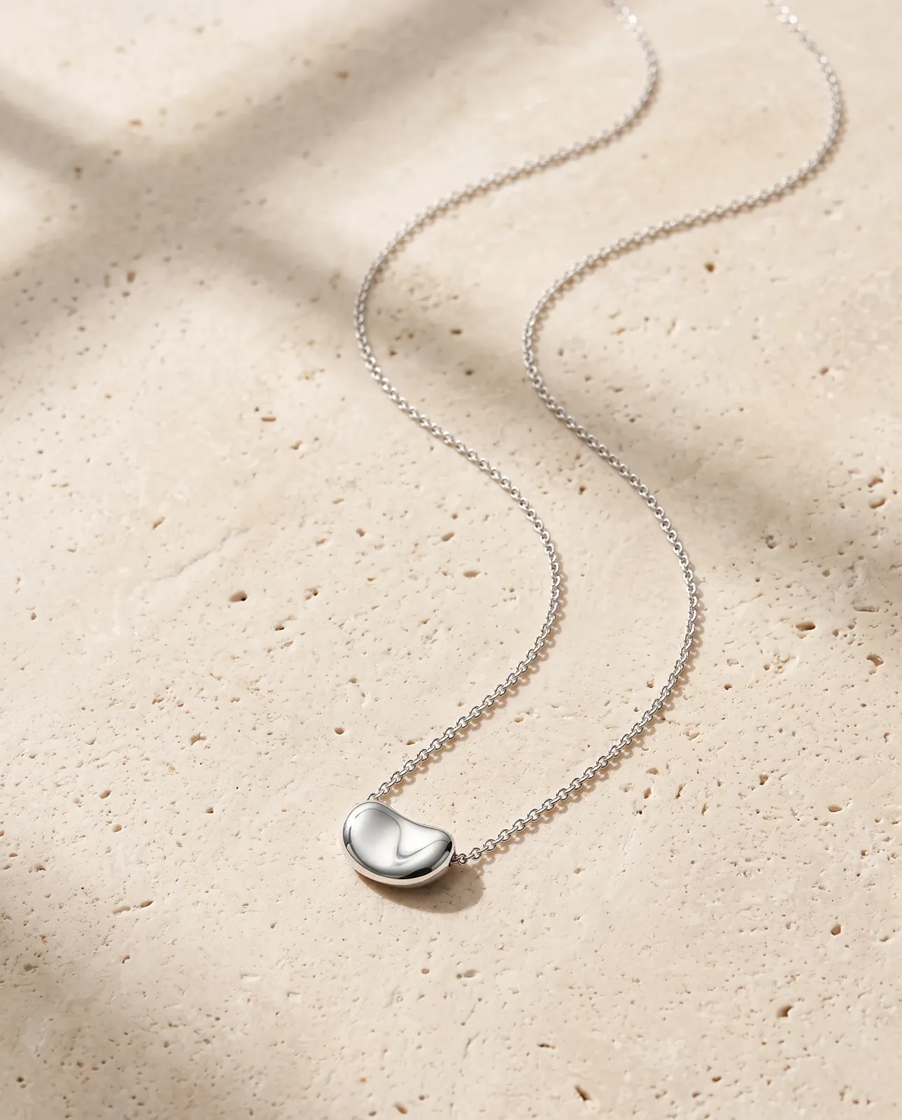 A silver pendant in a clean pale-stone product composition.